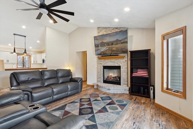 living area with lofted ceiling, ceiling fan, a fireplace, wood finished floors, and baseboards