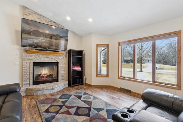 living room with vaulted ceiling, a fireplace, wood finished floors, and baseboards