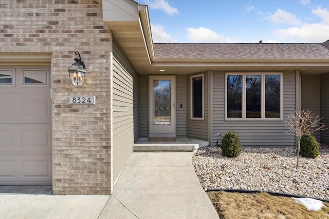 doorway to property featuring a shingled roof and an attached garage