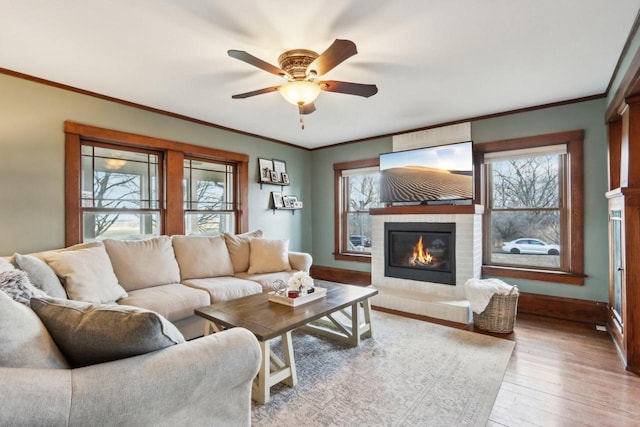 living room with baseboards, a glass covered fireplace, wood finished floors, and crown molding