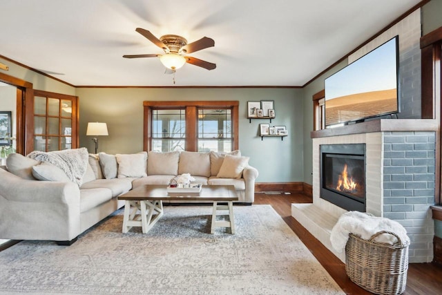 living room featuring a large fireplace, baseboards, ornamental molding, and wood finished floors