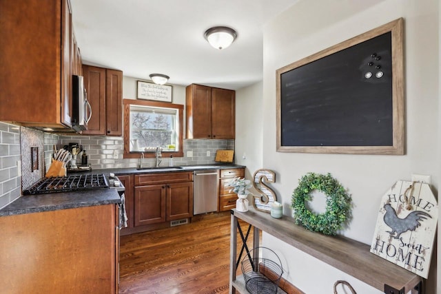 kitchen featuring tasteful backsplash, dark countertops, appliances with stainless steel finishes, dark wood-style flooring, and a sink