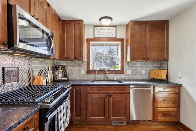 kitchen with stainless steel appliances, tasteful backsplash, visible vents, brown cabinetry, and a sink