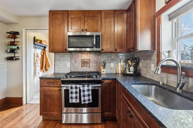 kitchen featuring stainless steel appliances, wood finished floors, a sink, decorative backsplash, and dark stone countertops