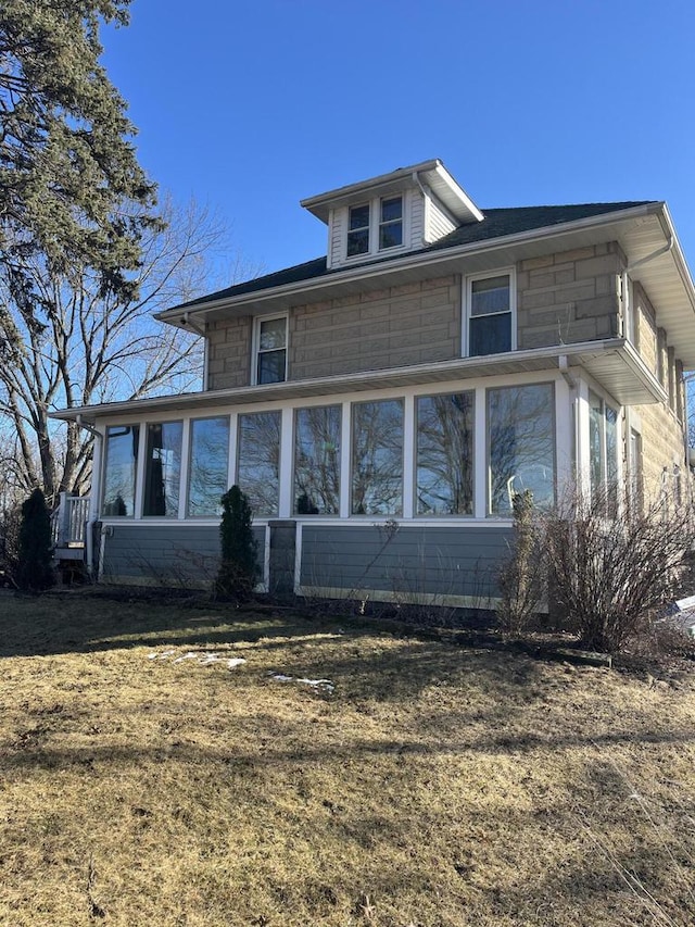 view of side of home with stone siding, a lawn, and a sunroom