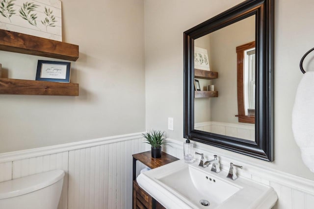 bathroom featuring a wainscoted wall, a sink, and toilet