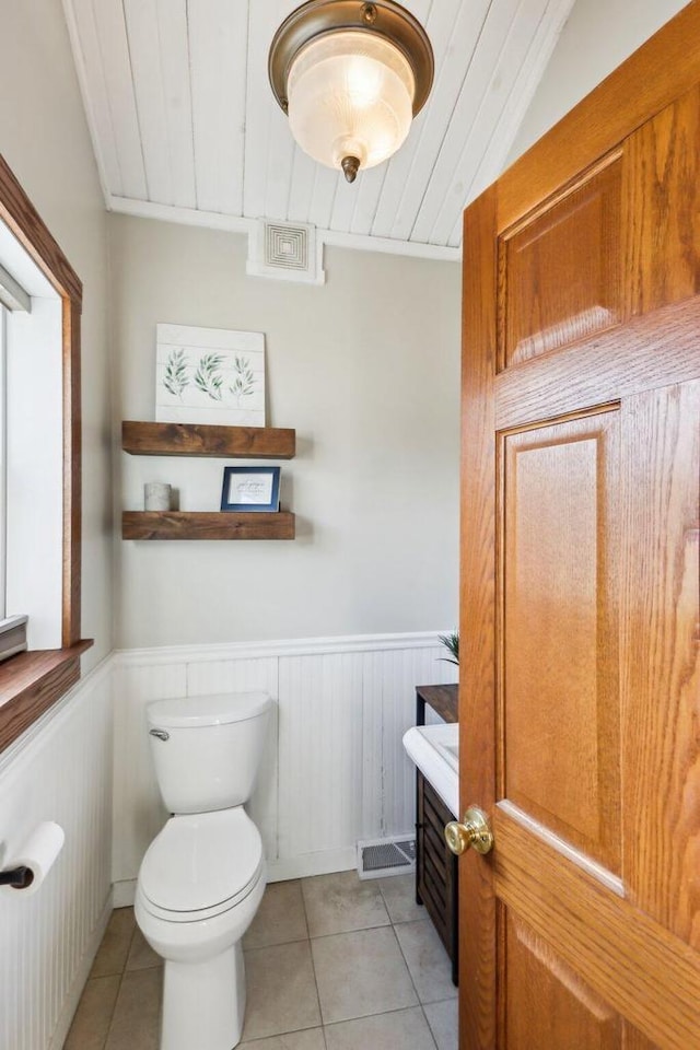 half bath with a wainscoted wall, wood ceiling, toilet, and tile patterned floors