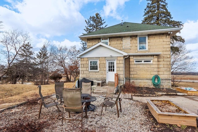 back of property with stone siding, a shingled roof, and a patio