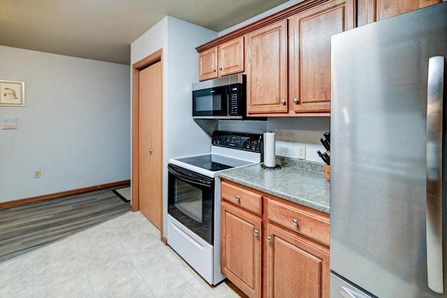 kitchen with baseboards, dark countertops, brown cabinets, stainless steel appliances, and light floors