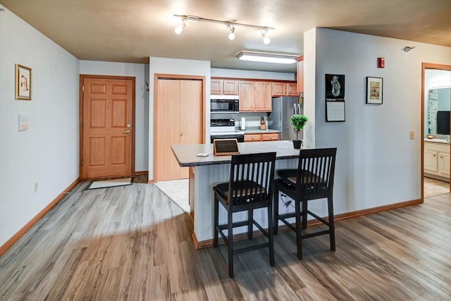 kitchen with a breakfast bar, freestanding refrigerator, light wood-style floors, black microwave, and range with electric stovetop