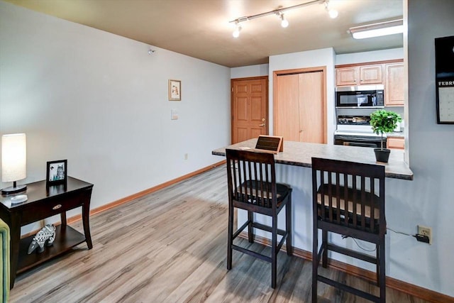 dining area with light wood-type flooring, baseboards, and track lighting