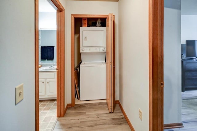 laundry area featuring laundry area, baseboards, stacked washer / dryer, light wood-style floors, and a sink