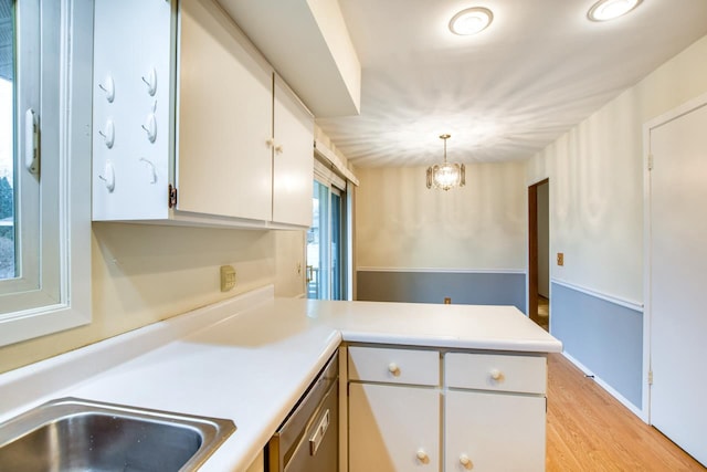 kitchen with a peninsula, white cabinets, light countertops, stainless steel dishwasher, and light wood-type flooring