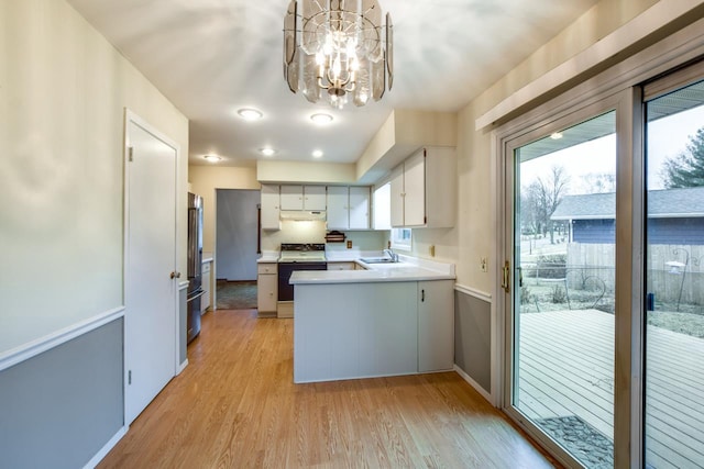 kitchen with electric range, light wood-style floors, high quality fridge, a sink, and a peninsula