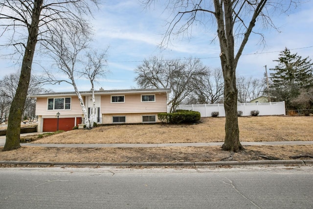 raised ranch featuring an attached garage, fence, and brick siding