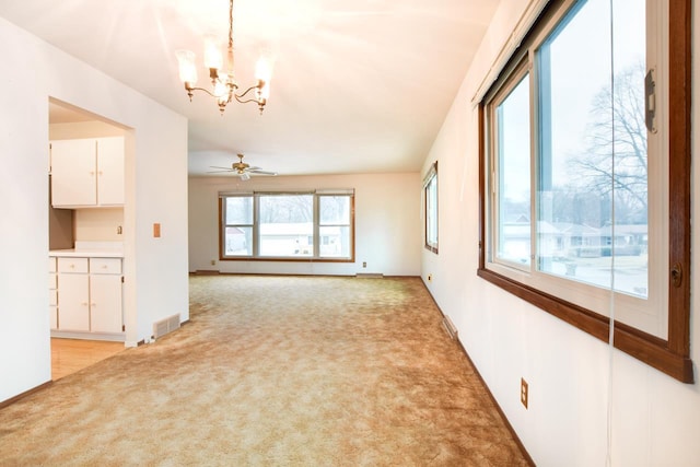 unfurnished living room with light carpet, ceiling fan with notable chandelier, and visible vents