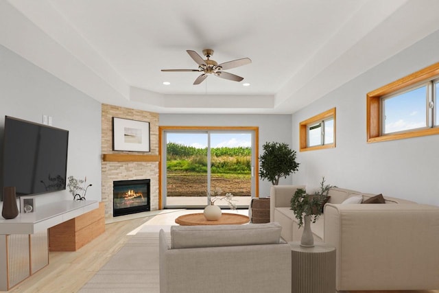 living area with a large fireplace, a tray ceiling, wood finished floors, and a ceiling fan