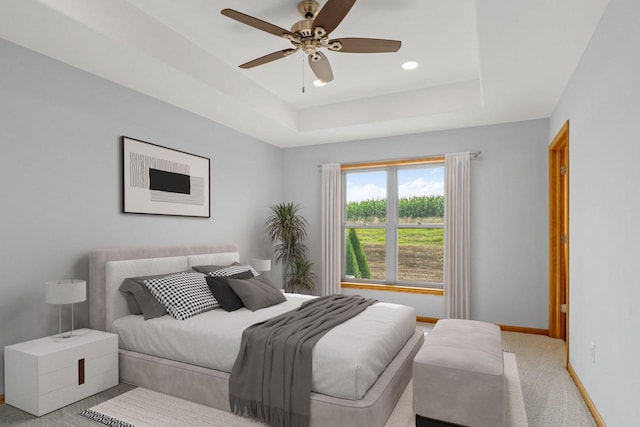 bedroom featuring a raised ceiling, light carpet, ceiling fan, and baseboards