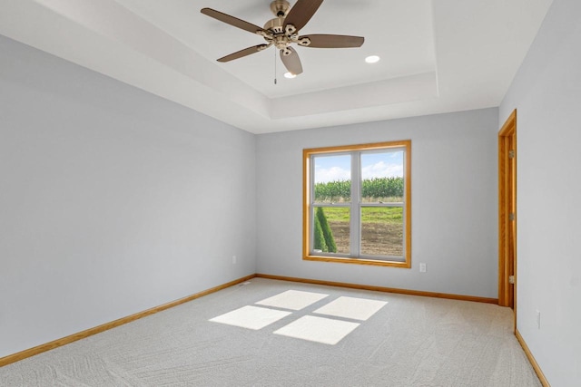 empty room featuring a ceiling fan, a raised ceiling, light carpet, and baseboards