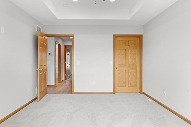 unfurnished bedroom featuring a raised ceiling, visible vents, light carpet, and baseboards