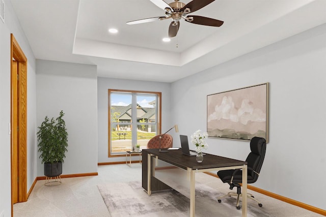 office space with a tray ceiling, light carpet, and baseboards