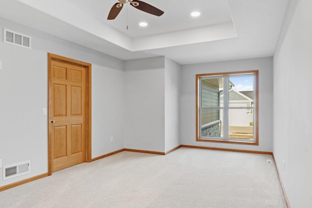 spare room with light carpet, a raised ceiling, visible vents, and baseboards