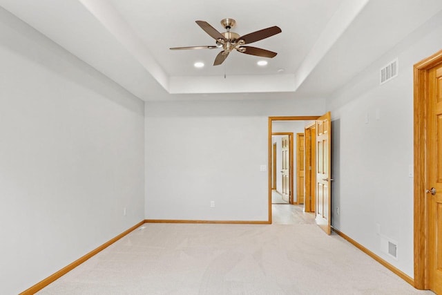 empty room featuring light carpet, visible vents, baseboards, and a raised ceiling