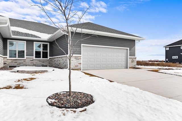 view of front of home with driveway, stone siding, an attached garage, and roof with shingles