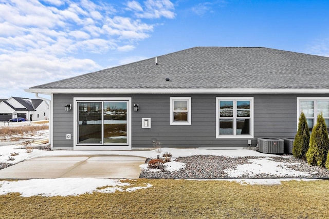 snow covered back of property featuring a shingled roof, cooling unit, and a patio area