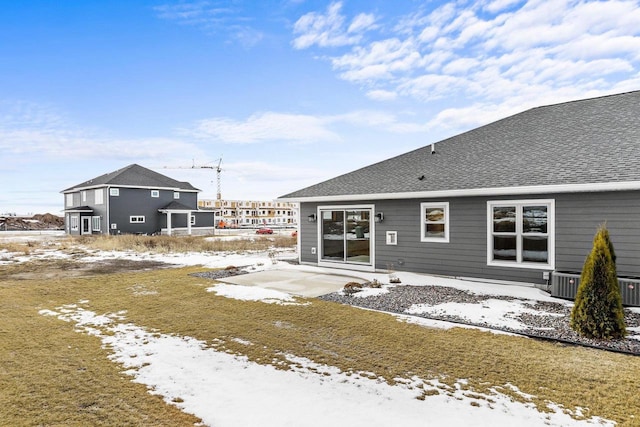 snow covered rear of property with central AC unit and roof with shingles