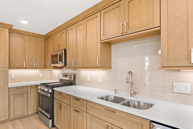 kitchen with stainless steel appliances, a sink, decorative backsplash, light stone countertops, and light wood finished floors