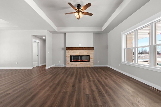 unfurnished living room featuring dark wood-style floors, a raised ceiling, visible vents, a stone fireplace, and baseboards