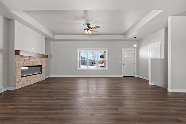 unfurnished living room featuring a fireplace, baseboards, a raised ceiling, and dark wood-type flooring