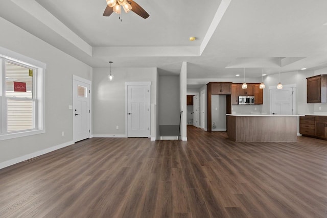 unfurnished living room with a ceiling fan, baseboards, a raised ceiling, and dark wood-style flooring