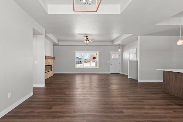 unfurnished living room with baseboards, a fireplace, a tray ceiling, and dark wood-type flooring