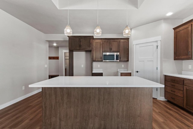 kitchen featuring a kitchen island, light countertops, stainless steel microwave, and hanging light fixtures