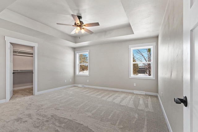 unfurnished bedroom featuring carpet, a raised ceiling, and multiple windows