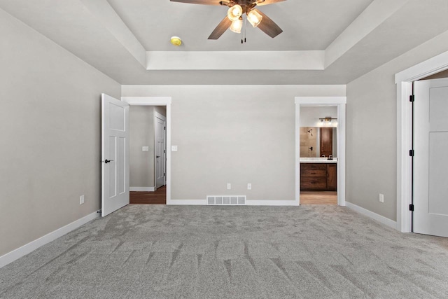 unfurnished bedroom with light carpet, baseboards, visible vents, a raised ceiling, and ensuite bath