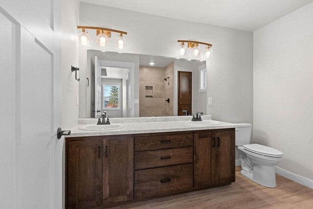 bathroom featuring double vanity, tiled shower, a sink, and toilet