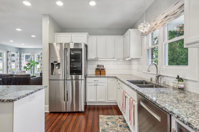 kitchen with light stone counters, stainless steel appliances, a sink, white cabinets, and decorative light fixtures