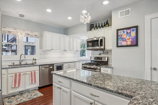 kitchen with white cabinetry, appliances with stainless steel finishes, a sink, and decorative light fixtures