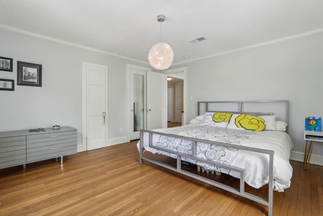 bedroom featuring ornamental molding, visible vents, baseboards, and wood finished floors