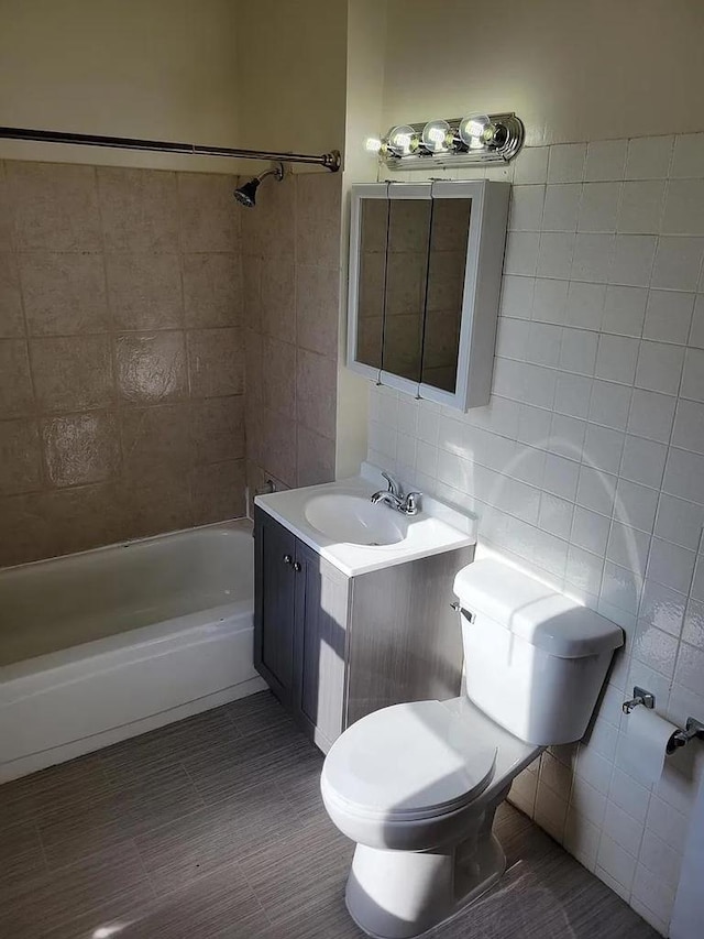 bathroom featuring toilet, bathing tub / shower combination, tile walls, and vanity