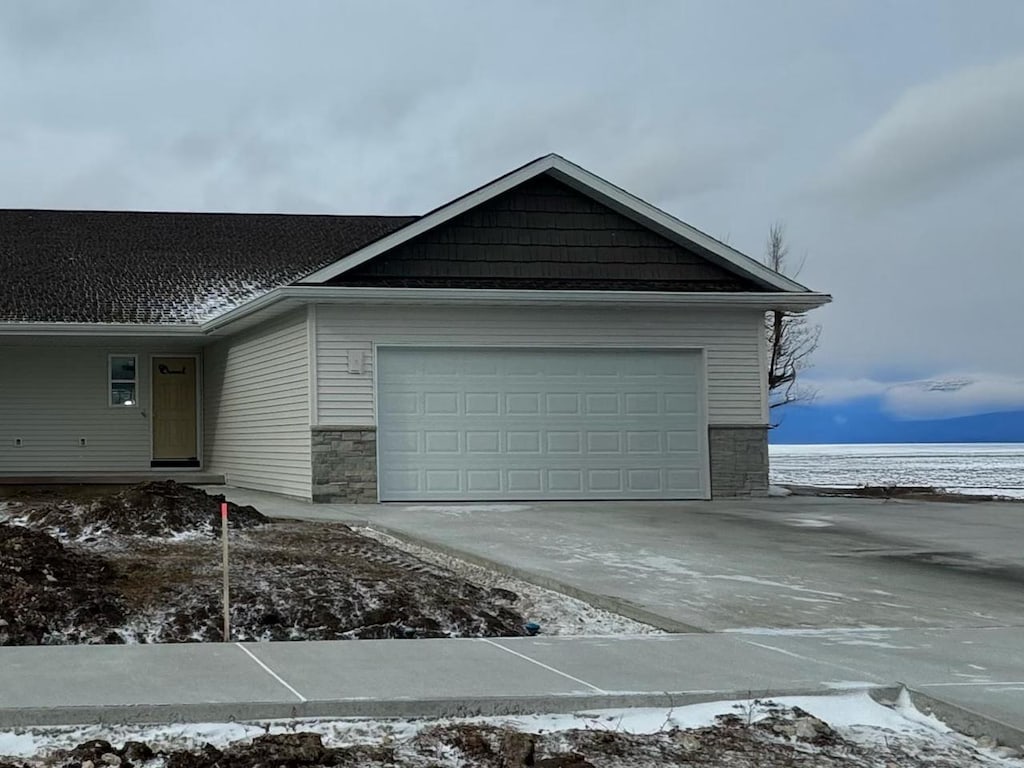 view of snowy exterior featuring a garage, stone siding, and driveway