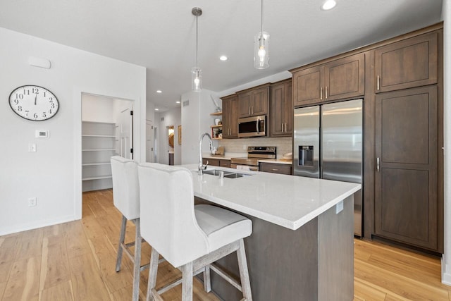 kitchen with a kitchen island with sink, light countertops, appliances with stainless steel finishes, open shelves, and pendant lighting