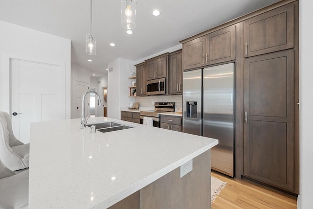 kitchen with light stone counters, a sink, appliances with stainless steel finishes, open shelves, and decorative light fixtures