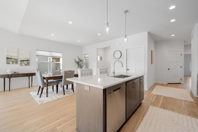 kitchen with decorative light fixtures, light countertops, stainless steel dishwasher, a sink, and an island with sink