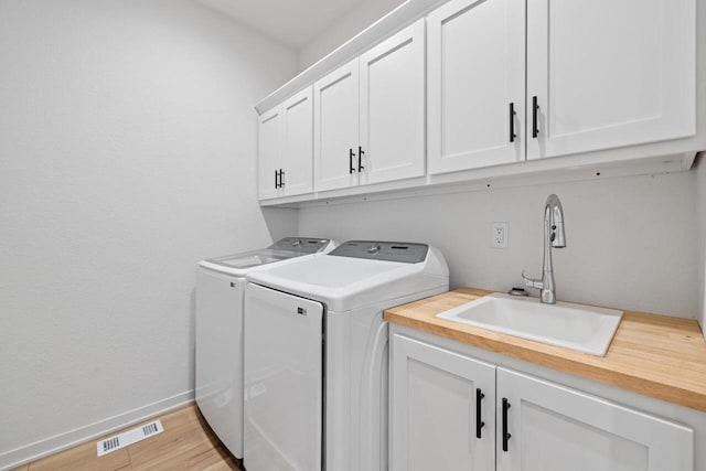 clothes washing area with cabinet space, baseboards, visible vents, washer and clothes dryer, and a sink