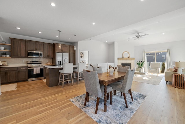 dining area featuring a ceiling fan, recessed lighting, a fireplace, and light wood finished floors