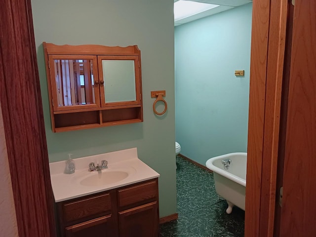 full bath featuring a skylight, baseboards, toilet, vanity, and a freestanding tub